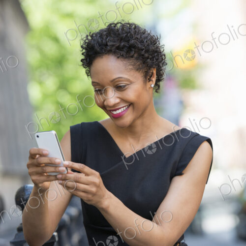 People on the move. A woman in a black dress on a city street, checking her phone. People on the move. A woman in a black dress on a city street, checking her phone.