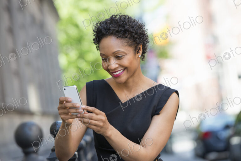 People on the move. A woman in a black dress on a city street, checking her phone.