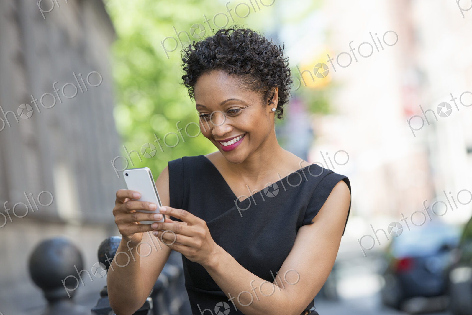 People on the move. A woman in a black dress on a city street, checking her phone.
