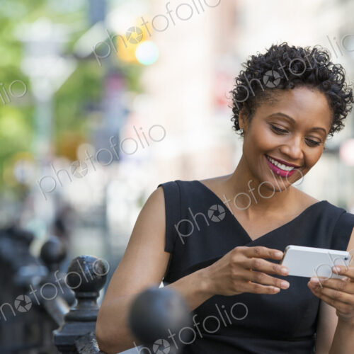 People on the move. A woman in a black dress on a city street, checking her phone. People on the move. A woman in a black dress on a city street, checking her phone.