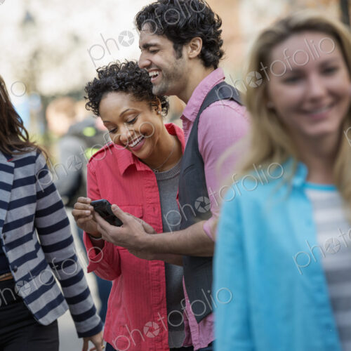People outdoors in the city in spring time. A group of men and women, two looking at a… People outdoors in the city in spring time. A group of men and women, two looking at a…