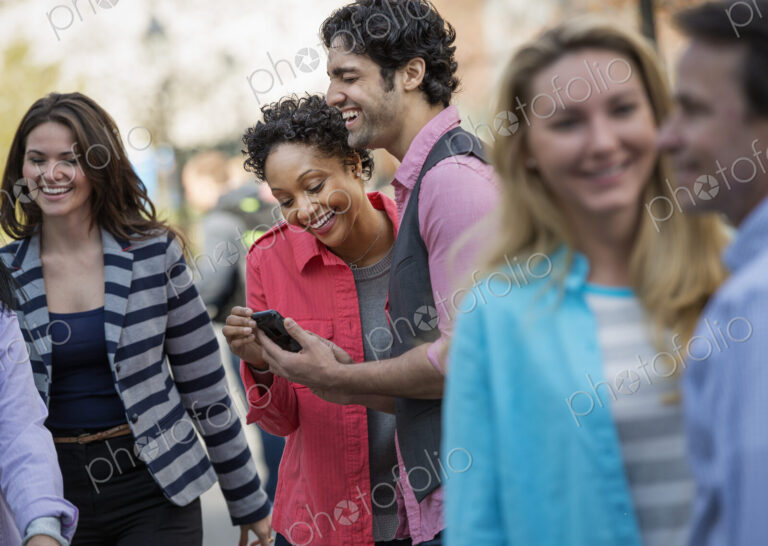 People outdoors in the city in spring time. A group of men and women, two looking at a…