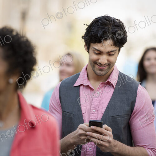 People outdoors in the city in spring time. A group of men and women. A man looking at…