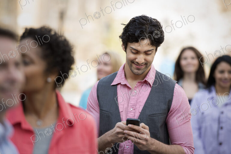 People outdoors in the city in spring time. A group of men and women. A man looking at…