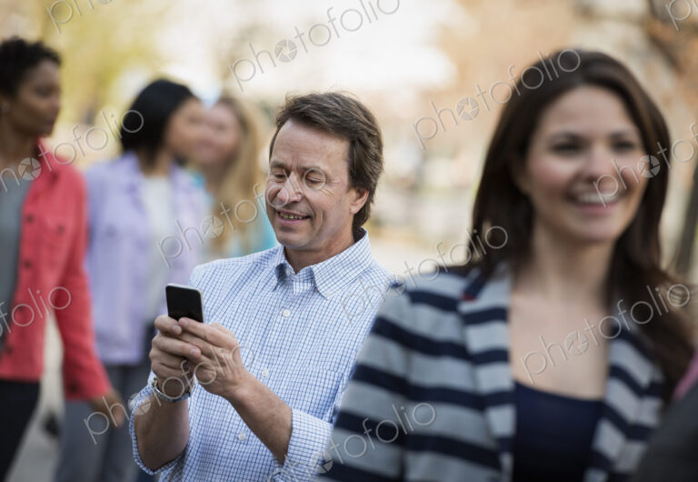 People outdoors in the city in spring time. A man checking his cell phone, among a…