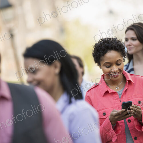 People outdoors in the city in spring time. A woman standing among a group checking…