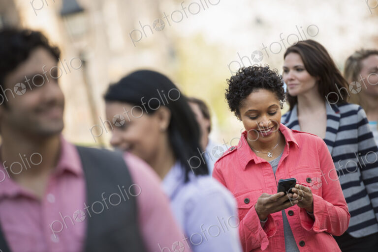 People outdoors in the city in spring time. A woman standing among a group checking…