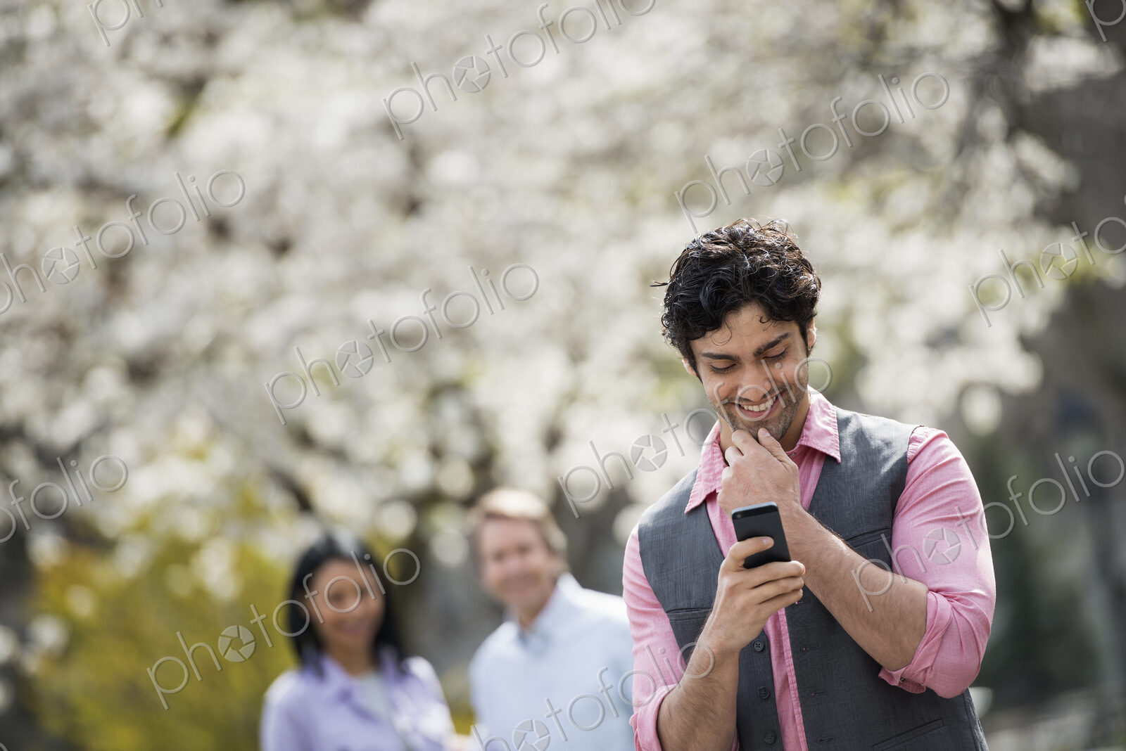 People outdoors in the city in spring time. Cherry blossom on the trees. A man…