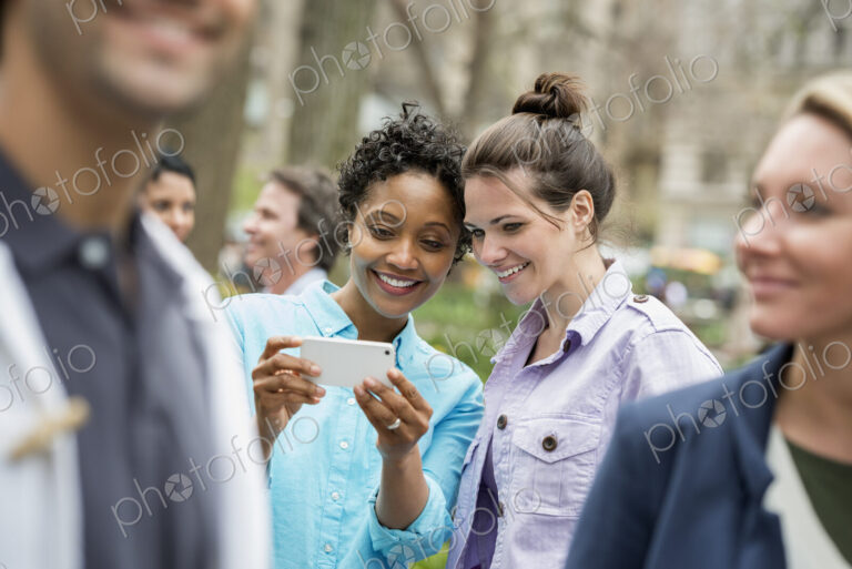 People outdoors in the city in spring time. New York City park. Two women in a group…