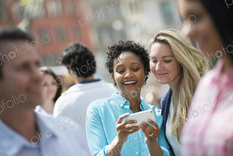 People outdoors in the city in spring time. New York City. A group of men and women,…