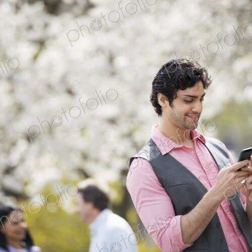People outdoors in the city in spring time. White blossom on the trees. A young man…