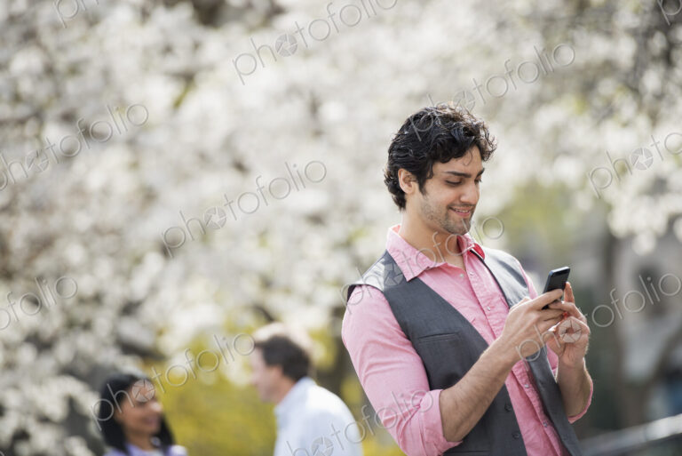 People outdoors in the city in spring time. White blossom on the trees. A young man…
