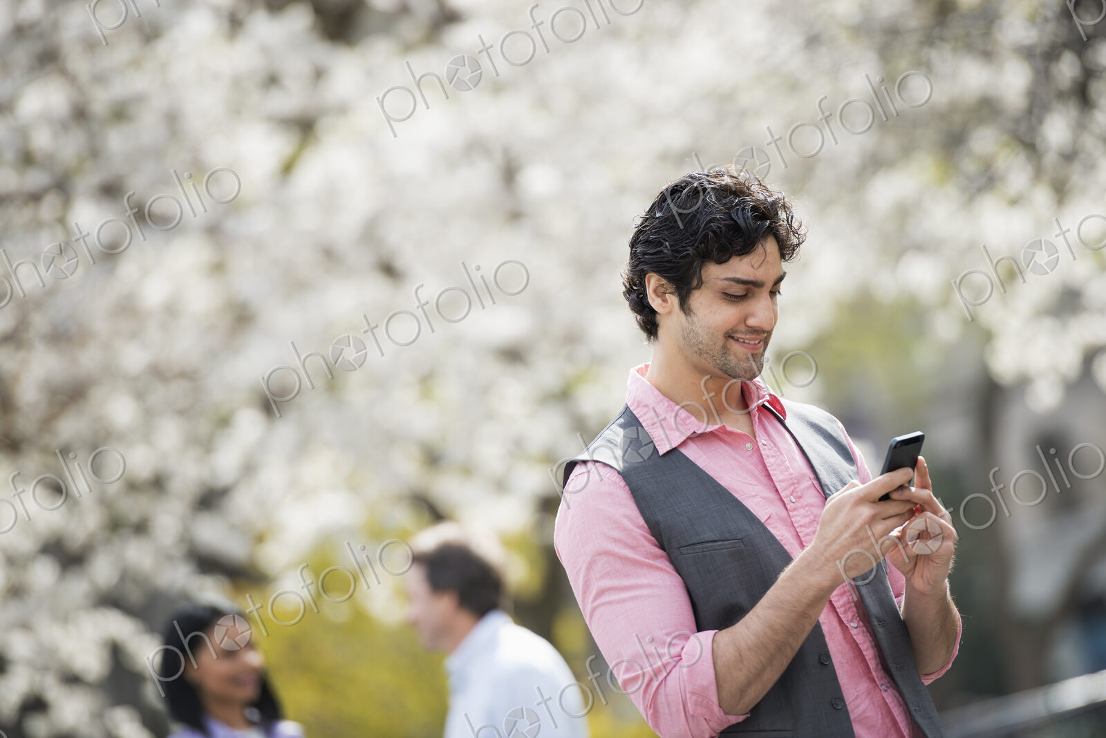 People outdoors in the city in spring time. White blossom on the trees. A young man…