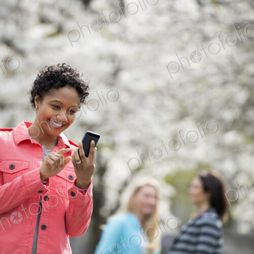 People outdoors in the city in spring time. White blossom on the trees. A young woman…