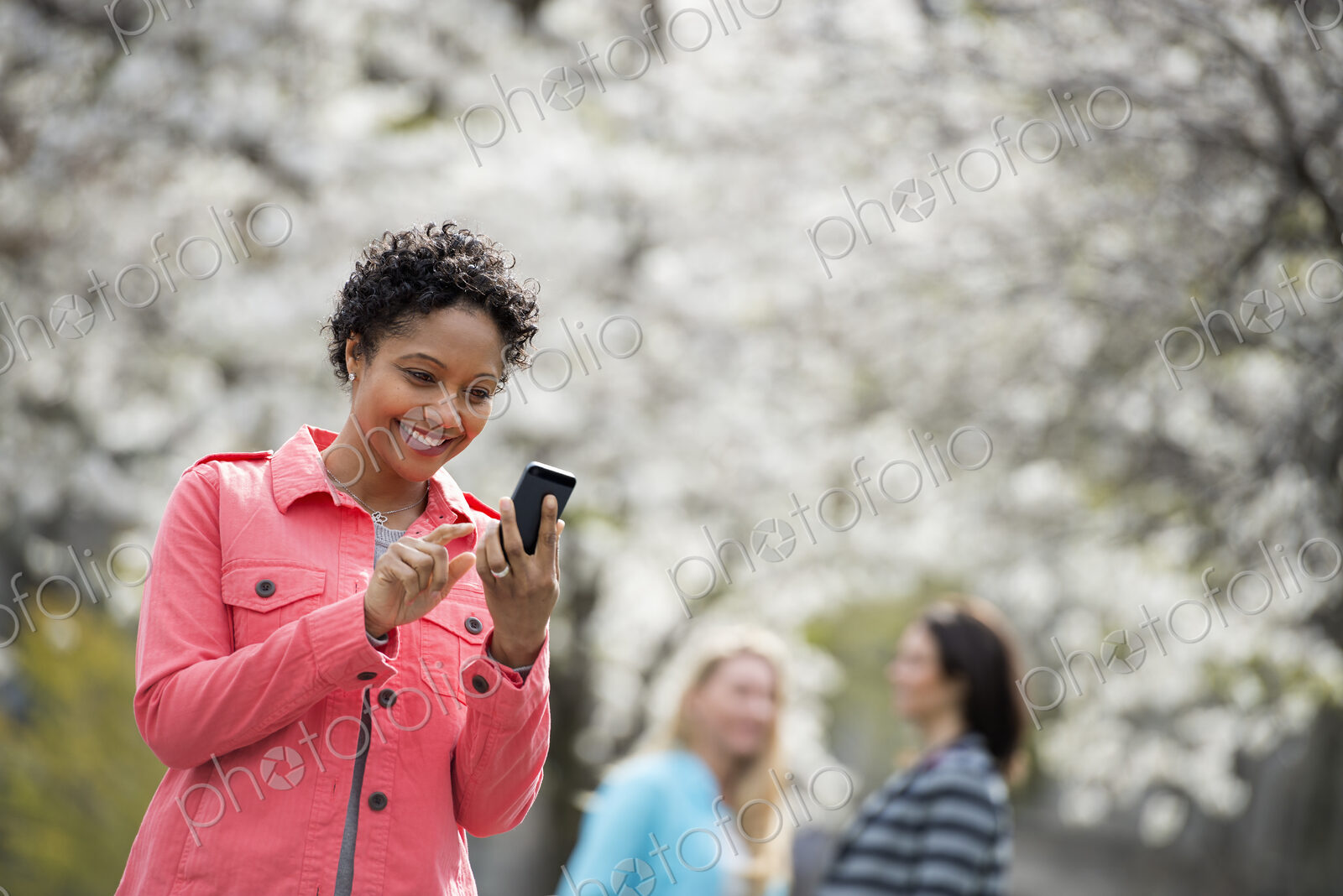 People outdoors in the city in spring time. White blossom on the trees. A young woman…