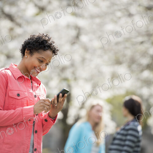 People outdoors in the city in spring time. White blossom on the trees. A young woman…