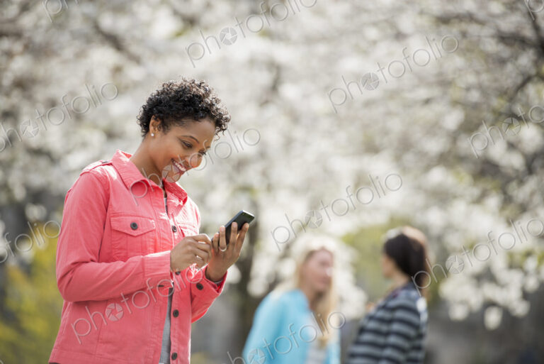 People outdoors in the city in spring time. White blossom on the trees. A young woman…