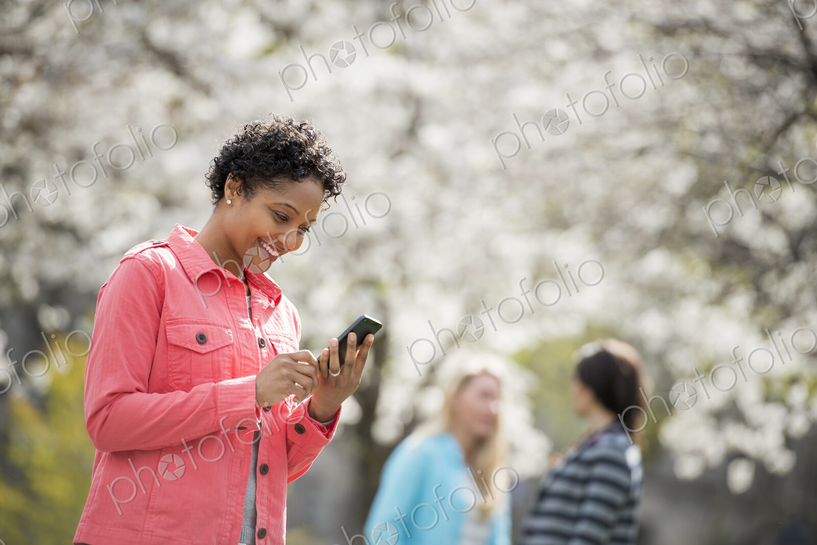 People outdoors in the city in spring time. White blossom on the trees. A young woman…