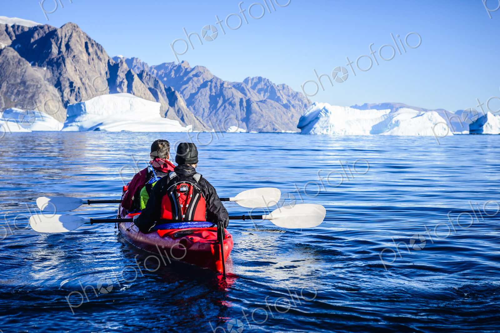 People paddling canoe towards glaciers in remote river