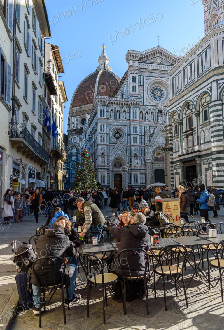 People sitting in a cafe near the Duomo in Florence, the baptistry with a marble…