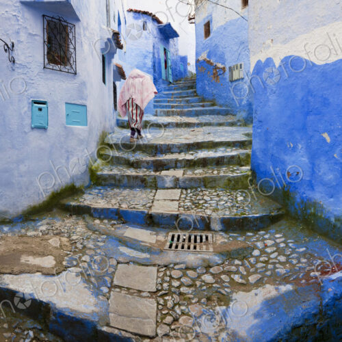 Person climbing cobblestone steps with blue washed traditional North African houses. Person climbing cobblestone steps with blue washed traditional North African houses.