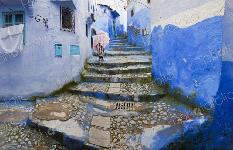 Person climbing cobblestone steps with blue washed traditional North African houses.