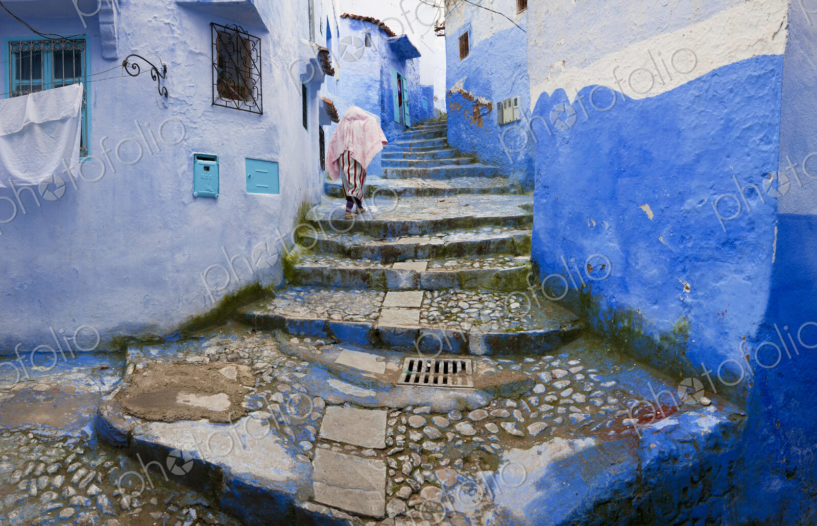 Person climbing cobblestone steps with blue washed traditional North African houses.