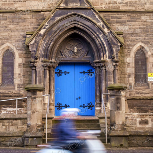 Person on a scooter driving past a gothic arch with bright blue door. Person on a scooter driving past a gothic arch with bright blue door.