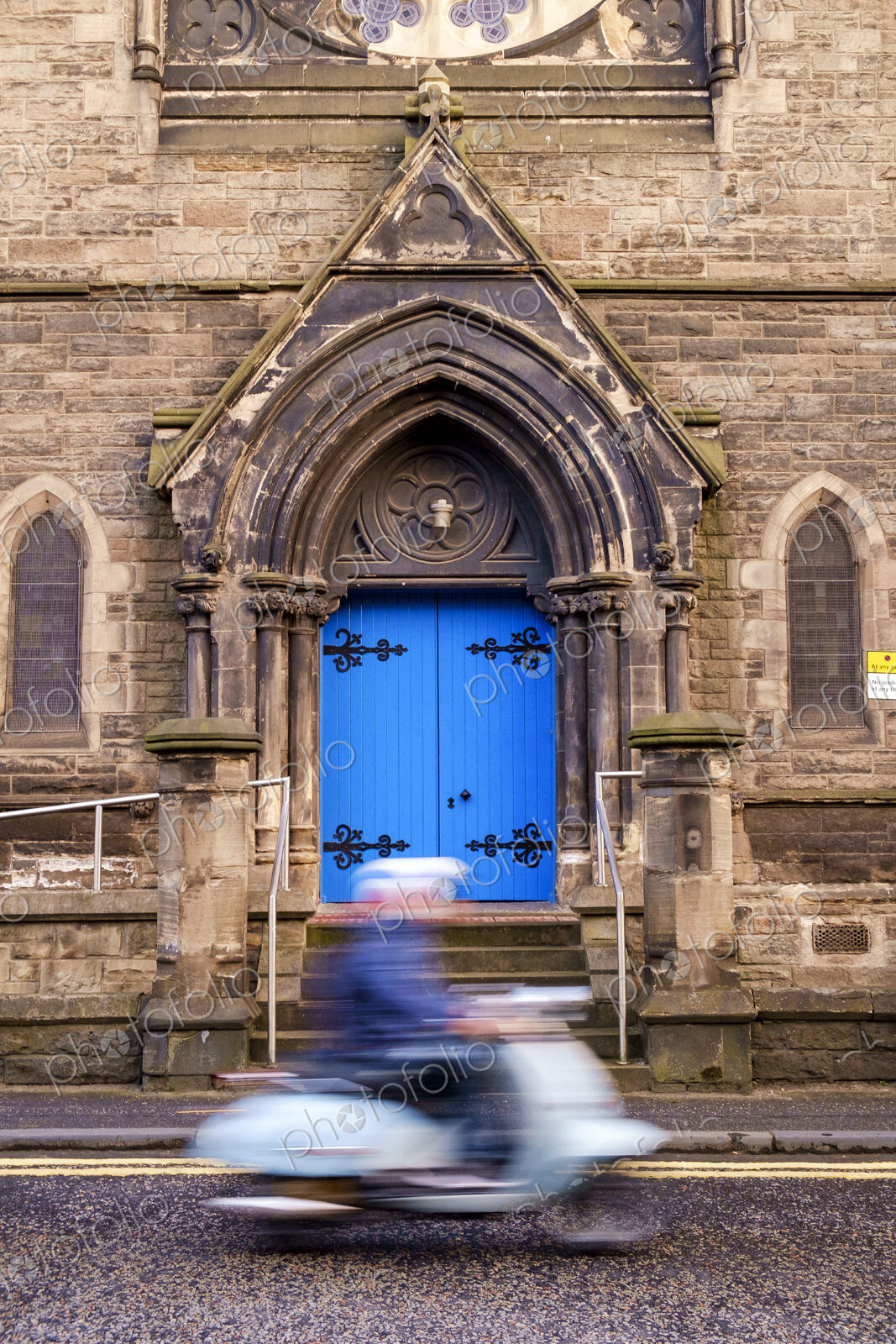 Person on a scooter driving past a gothic arch with bright blue door.