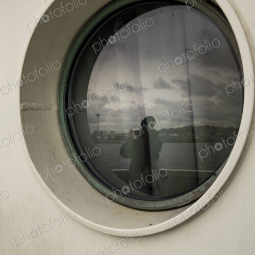 Person taking photo of Seattle's Space Needle, view through a Porthole on a Seattle ferry.
