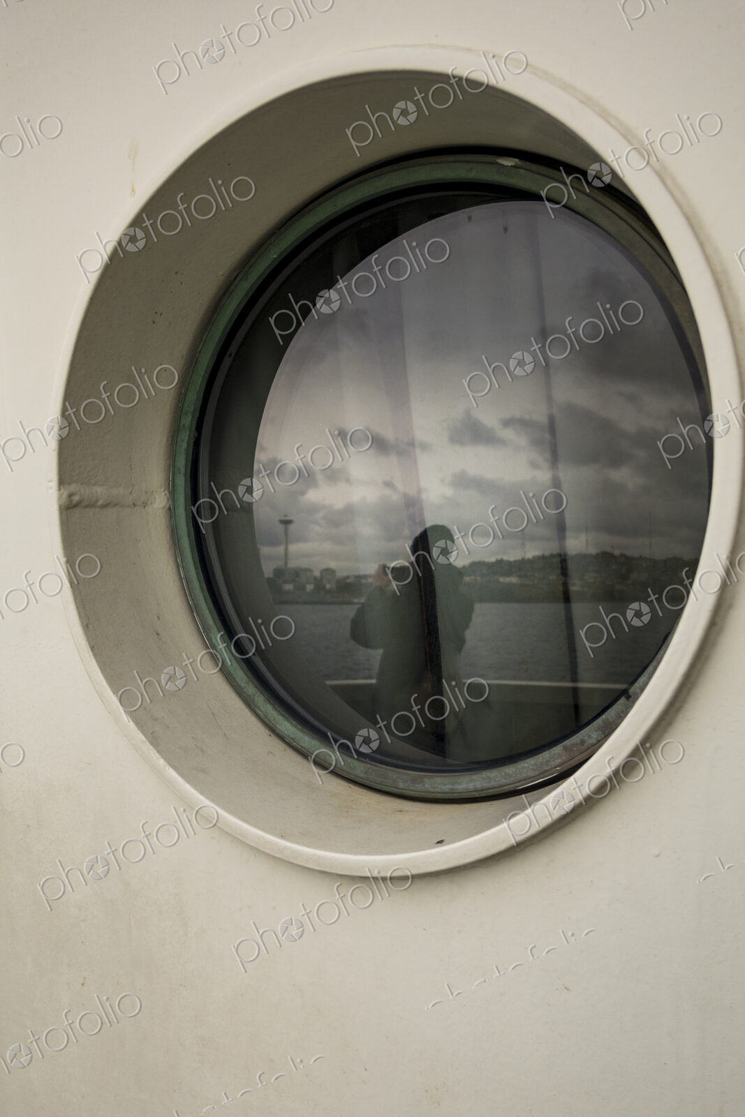 Person taking photo of Seattle’s Space Needle, view through a Porthole on a Seattle ferry.