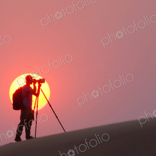 Photographer silhouetted in the setting sun in the Namib Desert, Namibia
