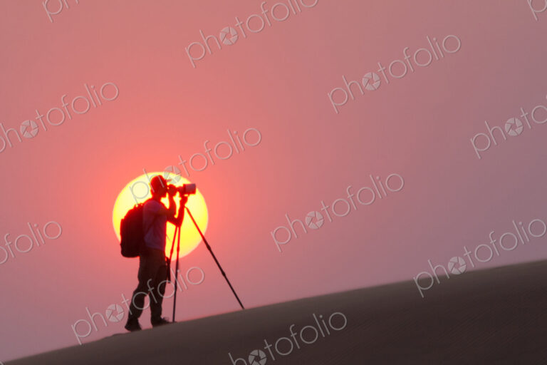 Photographer silhouetted in the setting sun in the Namib Desert, Namibia