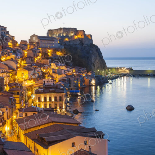 Picturesque coastal town at dusk, with illuminated castle on cliff. Picturesque coastal town at dusk, with illuminated castle on cliff.