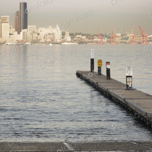Pier into water on urban waterfront with skyscrapers beyond.