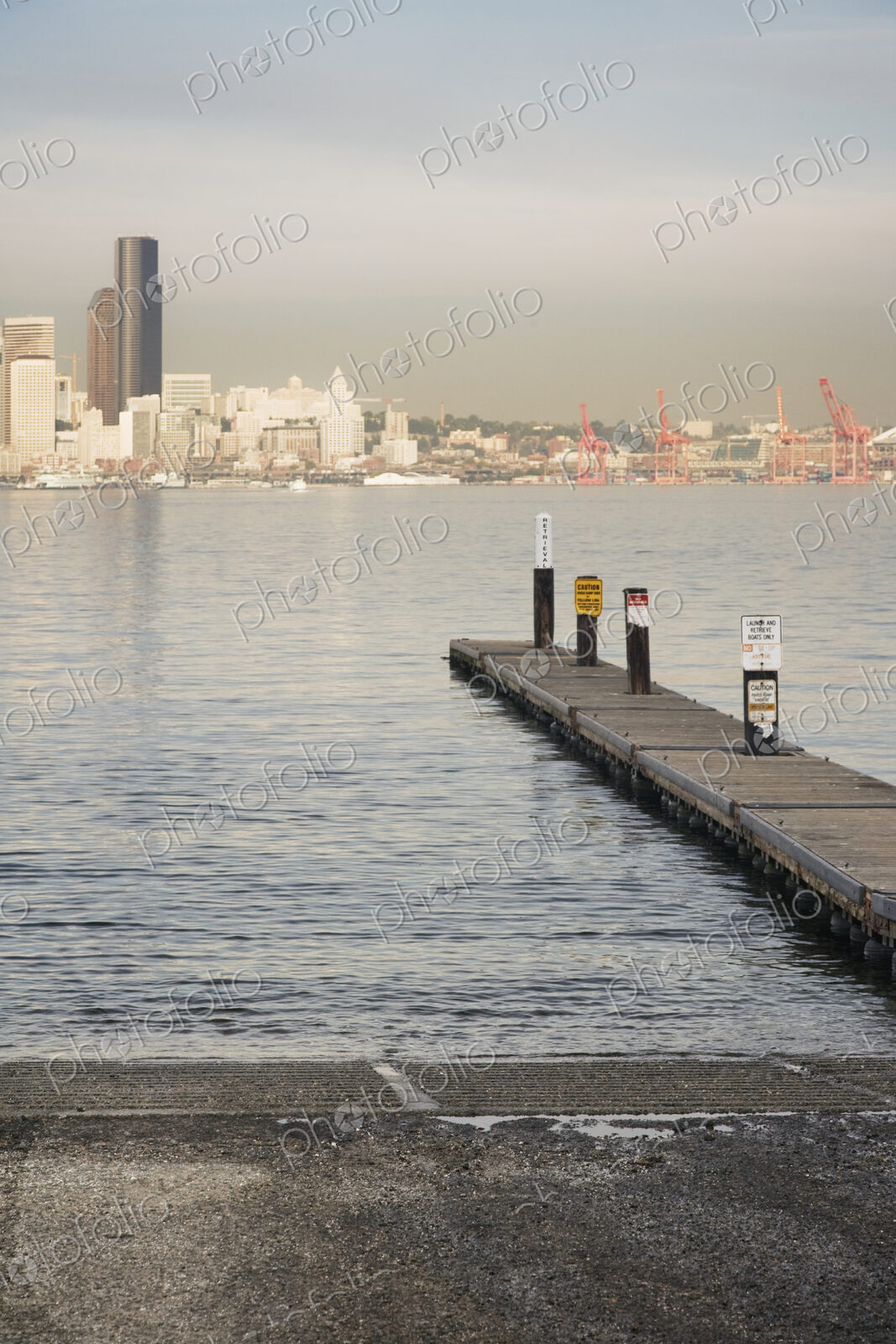 Pier into water on urban waterfront with skyscrapers beyond.
