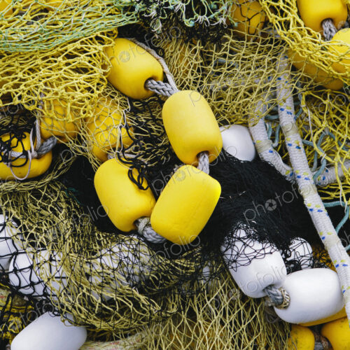 Pile of commercial fishing nets, with yellow and white floats, on the quayside at…