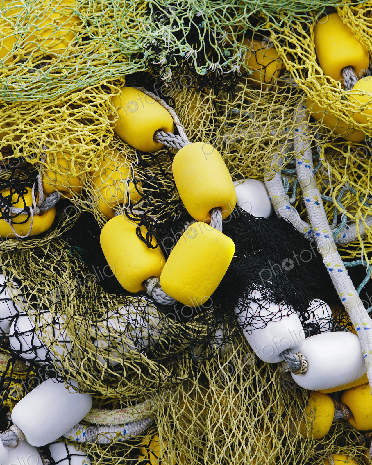 Pile of commercial fishing nets, with yellow and white floats, on the quayside at…