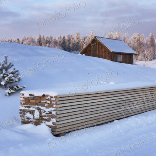 Piled timber and small wooden house in winter snow Piled timber and small wooden house in winter snow