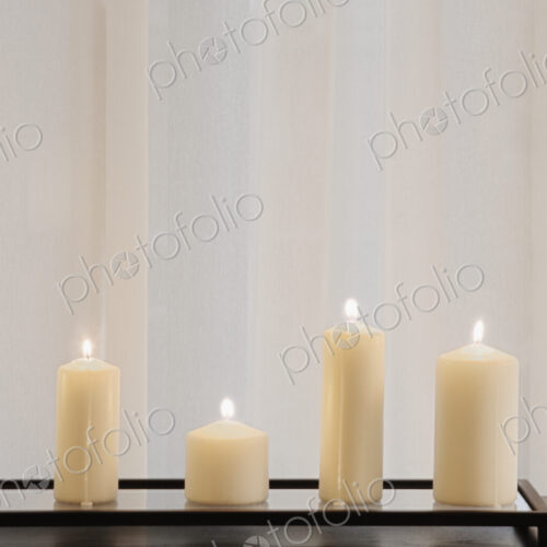 Pillar candles lit and lined up in front of curtain.