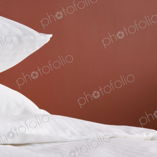 Pillows in white covers, against a red wall
