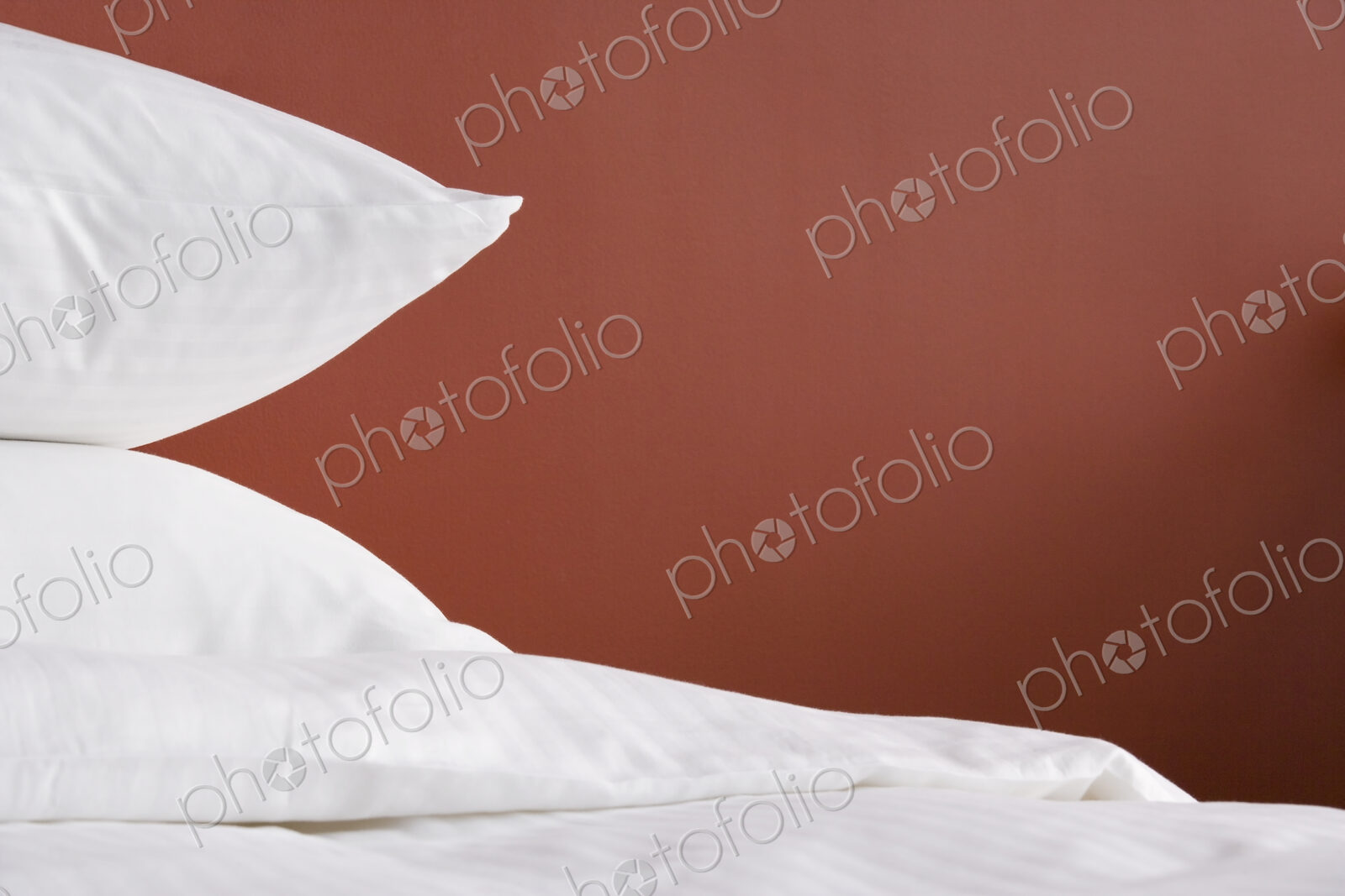 Pillows in white covers, against a red wall