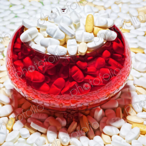 Pills, capsules, white and brown, spread out and in a red glass bowl. Pills, capsules, white and brown, spread out and in a red glass bowl.