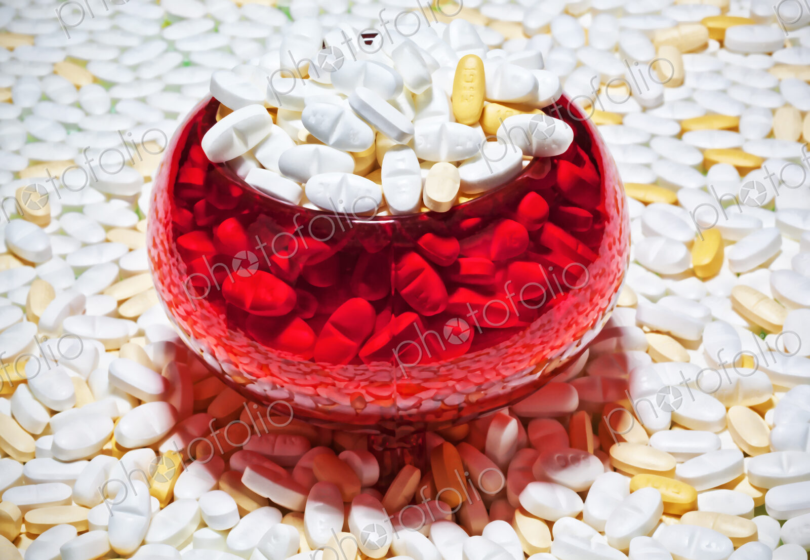 Pills, capsules, white and brown, spread out and in a red glass bowl.