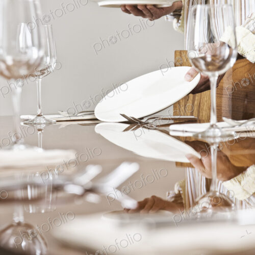 Place settings being arranged on a dining room table.
