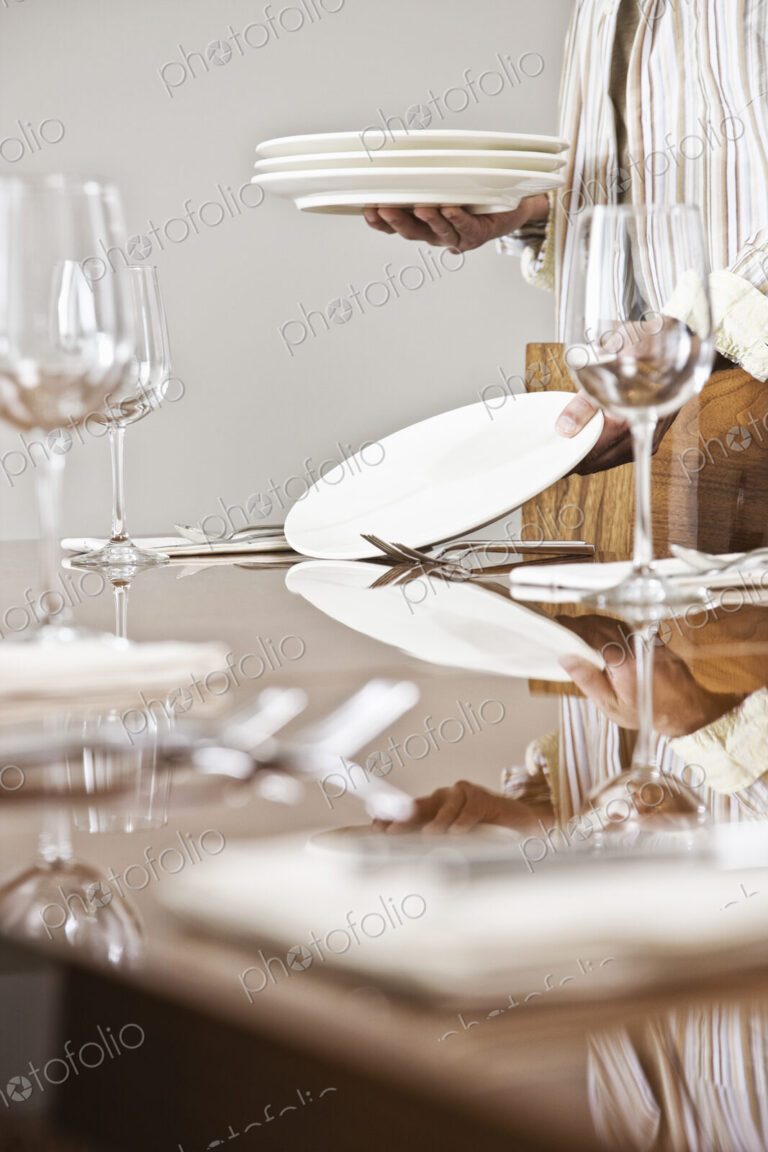 Place settings being arranged on a dining room table.