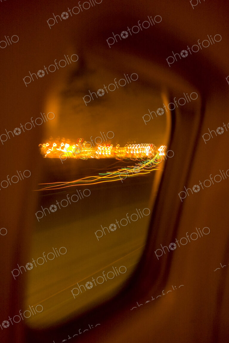 Plane window view of landing on a runway, lights beside the runway.