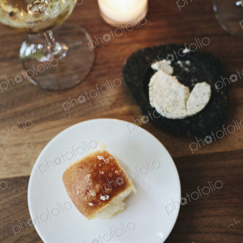 Plate with a bread roll, herb butter and glass of wine at a city restaurant.