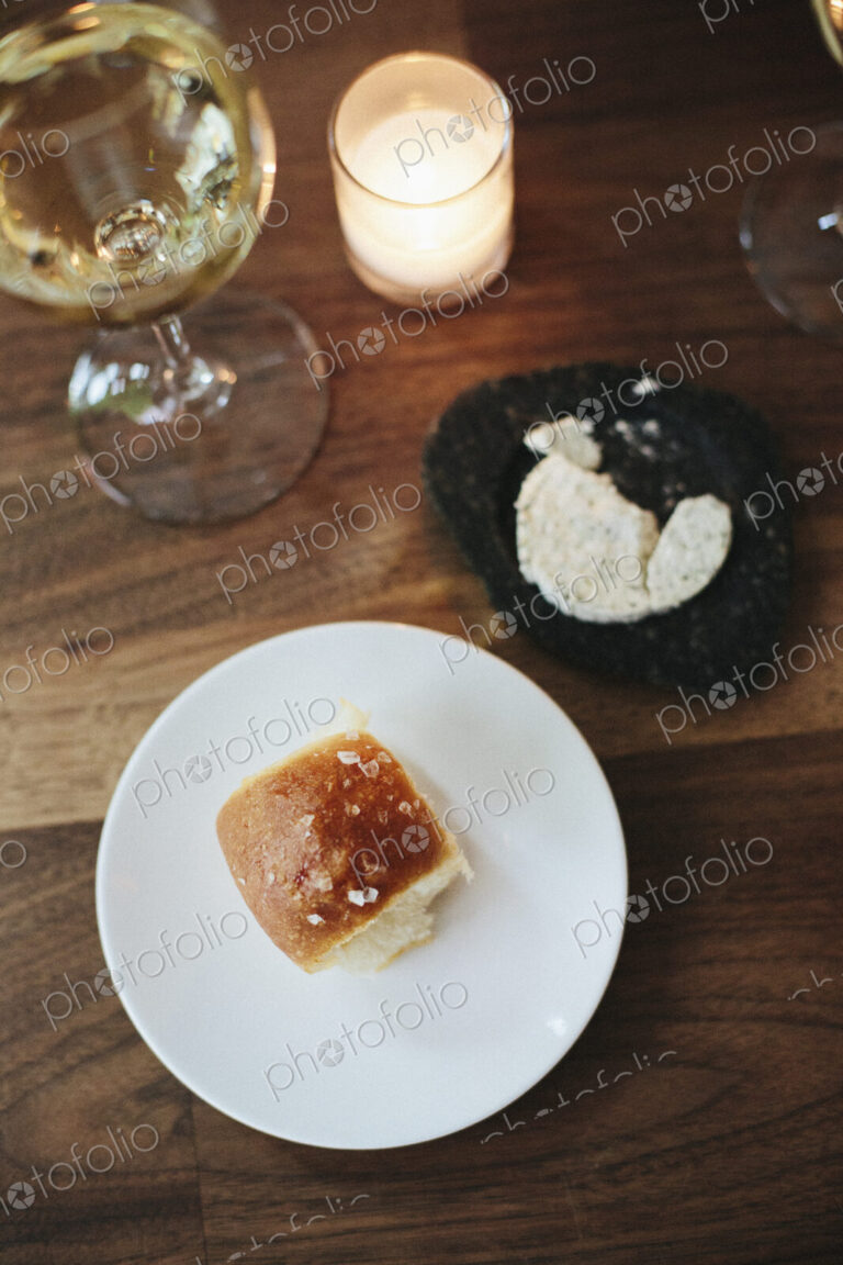 Plate with a bread roll, herb butter and glass of wine at a city restaurant.