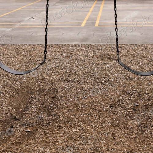Playground swings, two empty children's swings, above a bark base. Playground swings, two empty children's swings, above a bark base.
